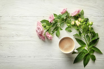 Beautiful rose flowers with cup of coffee on wooden background, top view