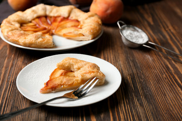 Plate with piece of delicious peach galette on wooden table