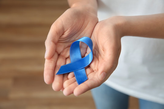 Woman holding blue ribbon, closeup. Cancer concept