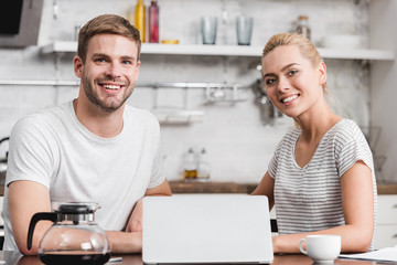 happy young couple using laptop and smiling at camera together