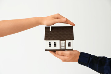 Man and woman holding house model on light background. Mortgage concept