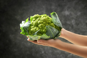 Woman holding green cauliflower on dark background