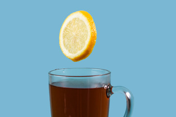 A fresh juicy yellow lemon with a sugar cube flies into a cup of Ceylon black tea on a blue background.