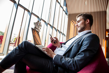 Young businessman working on laptop, sitting in hotel lobby waiting for someone.