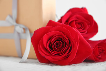 Beautiful red roses and gift on light table, closeup