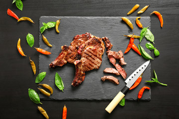 Tasty grilled steaks with chili peppers and basil on slate plate