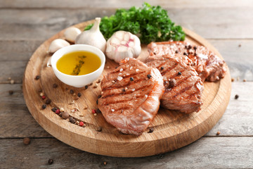 Board with delicious grilled steaks, oil and spices on wooden table