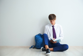 Teenage boy with book sitting on floor near light wall