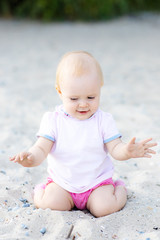 Kids lifestyle outdoor. Happy cute girl in bikini and panama playing with sand on the beach of sea. Summer vacation and family travel concept. Little baby girl sitting on the sand near the sea