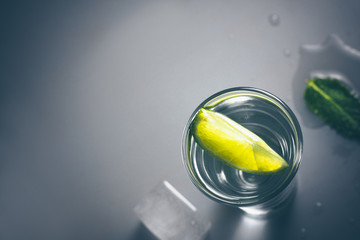 Top view of a glass of tequila with a lime slice and ice on a glass table