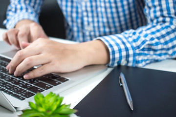 Close up the hands of a man wearing a blue plaid shirt typing on the keyboard laptop. Business Concepts.
