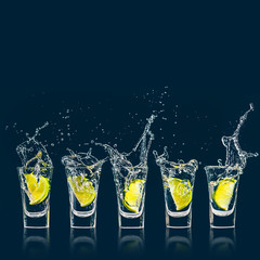 A piece of lime falls with a splash in a shot glass of vodka - obrazy, fototapety, plakaty