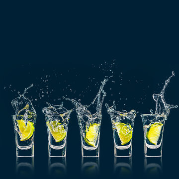 A piece of lime falls with a splash in a shot glass of vodka