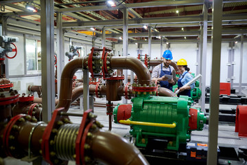 Wide angle  portrait of two factory workers using digital tablet while working with piping and machines in modern workshop, copy space