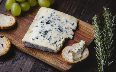 Fototapeta na wymiar Roquefort Käse auf einem Holztisch mit Trauben, Rosmarien und Brot