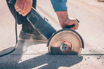 The worker saws the asphalt with an angular grinder with a diamond disc before carrying out repair...
