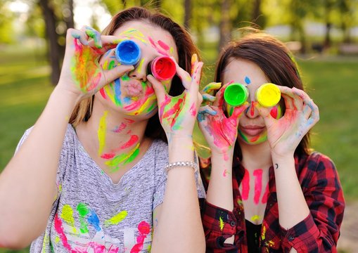 two young cheerful friends smeared with colored paints in the park on a background of nature and greens