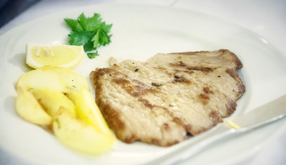 A dish with a well cooked steak with potatoes, lemon and parsley.
