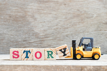 Toy forklift hold letter block y to complete word story on wood background
