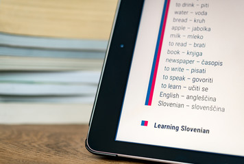 Learning Slovenian using a tablet with books in the background.