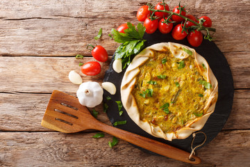Spicy potato savory tart with vegetables and herbs close up on the table. horizontal top view