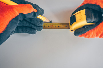 First person view: a tiler in gloves puts a mark on a white wall using a tape measure and a pencil