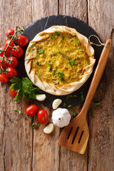 Spicy potato savory tart with vegetables and herbs close up on the table. vertical top view