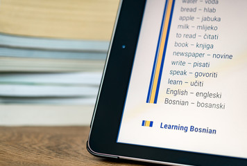 Learning Bosnian using a tablet with books in the background.