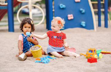 Interesting game. Two cute Caucasian and hispanic latin babies children sitting in sandbox playing...