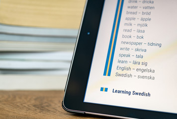 Learning Swedish using a tablet with books in the background.