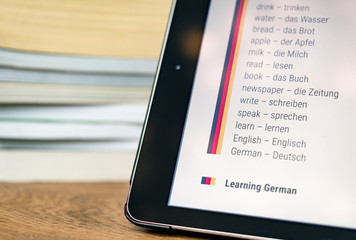 Learning German using a tablet with books in the background.