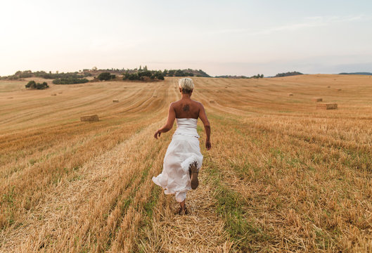 Young blond woman with white dress and short cut posing and walking by a dry straw countryside in a sunset of summer