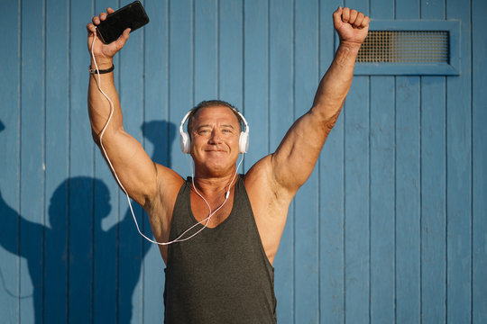 Strong older man poses with headphones on blue cabin background.