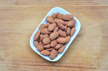 Salted roast organic almonds on a white plate on wood background
