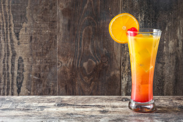 Tequila sunrise cocktail in glass on wooden table. Copyspace