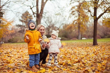 A young beautiful mother and two small children are walking around the autumn park. Mom and two small children play. Warm winter. Bright autumn.