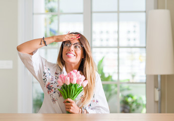 Young woman at home holding pink tulips flowers stressed with hand on head, shocked with shame and surprise face, angry and frustrated. Fear and upset for mistake.