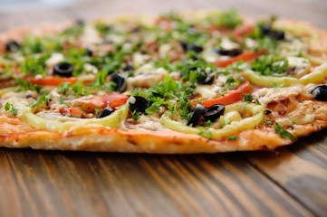 Preparation of homemade pizza with salami, mushrooms, olives, tomatoes and greens