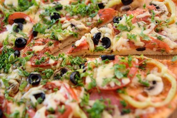 Preparation of homemade pizza with salami, mushrooms, olives, tomatoes and greens