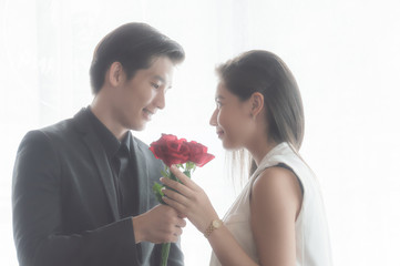Couple are romantic in love, and holding red rose flower in her hand, withe blurred white background