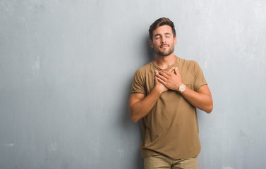 Obraz premium Handsome young man over grey grunge wall smiling with hands on chest with closed eyes and grateful gesture on face. Health concept.