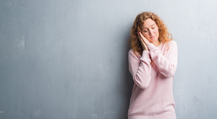 Fototapeta premium Young redhead woman over grey grunge wall wearing pink sweater sleeping tired dreaming and posing with hands together while smiling with closed eyes.
