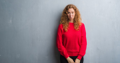 Young redhead woman over grey grunge wall wearing red sweater depressed and worry for distress, crying angry and afraid. Sad expression.