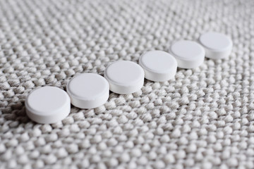 white round tablets or vitamins stacked in one row on a knitted background close-up