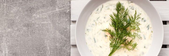 Panorama of concrete empty copy space kitchen worktop with cucumber soup in a white plate on a wooden placemat as seen from above