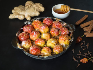 Baked apples in a frying pan with ginger, cinnamon, honey and pepper on a black background.