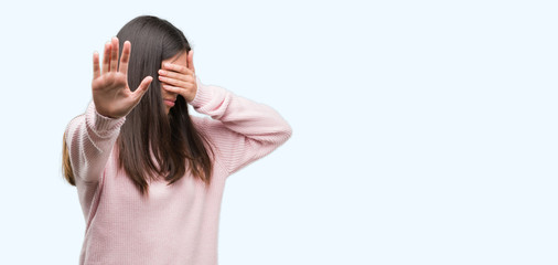 Young beautiful hispanic woman wearing a sweater covering eyes with hands and doing stop gesture with sad and fear expression. Embarrassed and negative concept.