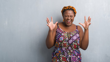 Young african american woman over grey grunge wall wearing orange braids celebrating mad and crazy...