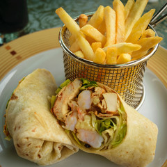 Plated shrimp and chicken wrap cut in half with french fries in small mesh wire basket. Hotel...