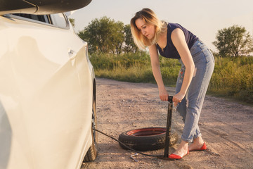 Young beautiful girl is shaking a pump with a wheel of a car on a country road in the rays of the...